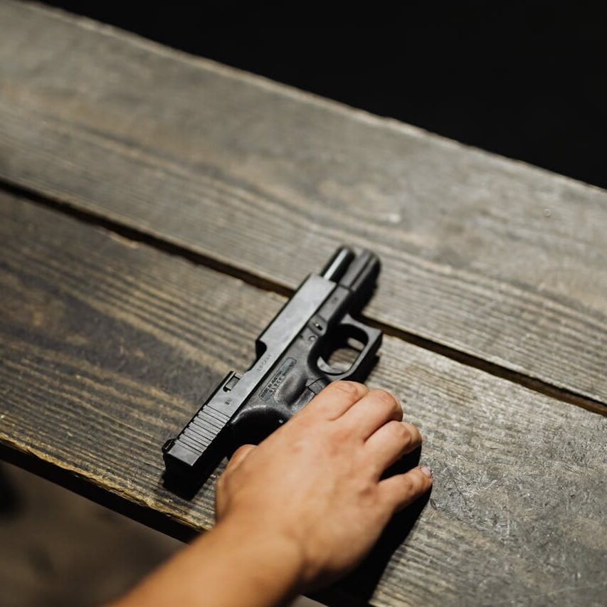 Photo of a handgun and a person's hand on a wooden table, part of firearm safety and handgun license training in Waco.